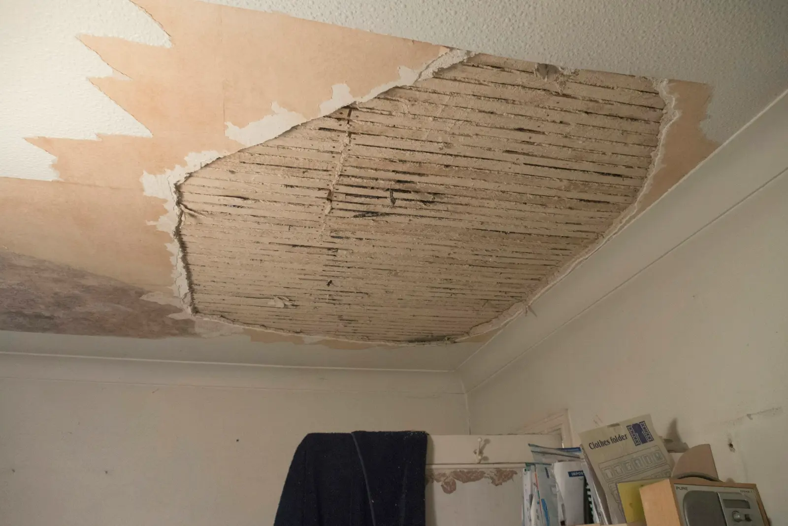 Plafond d’une pièce habitée dont une plaque d’enduit est tombée, découvrant le lattis de bois.