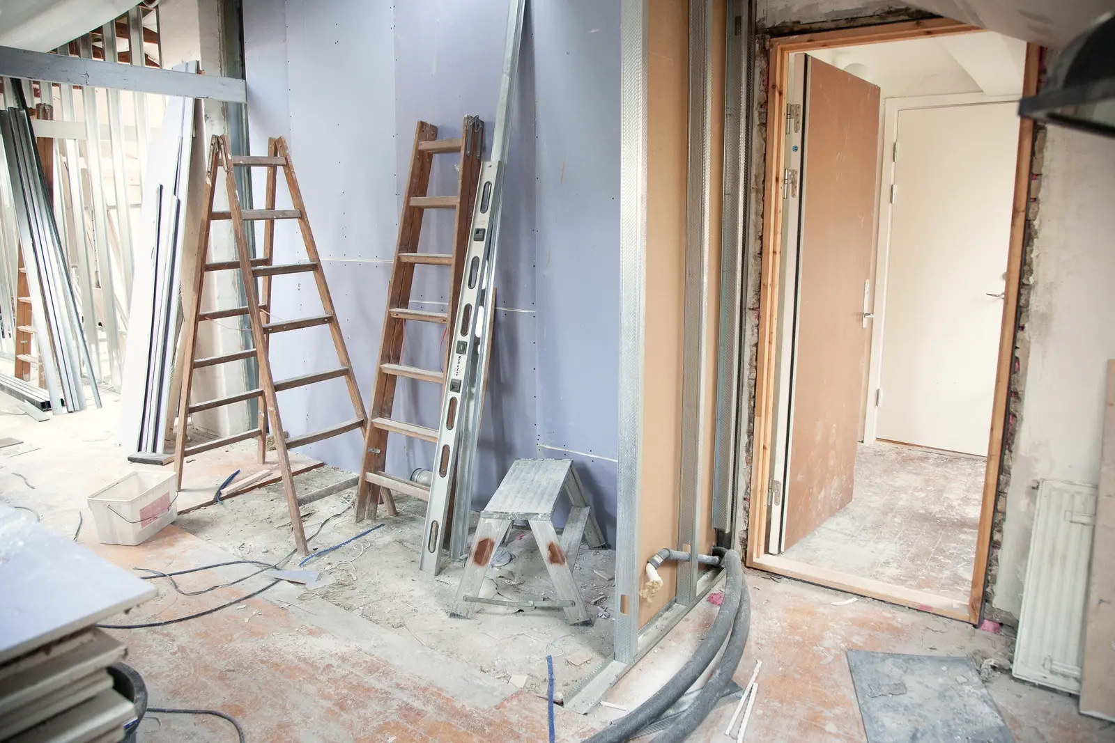 Chantier interrompu : ossature métallique montée, plaques de plâtre posées, huisserie de porte en place et gaine laissée au sol sur les tommettes.