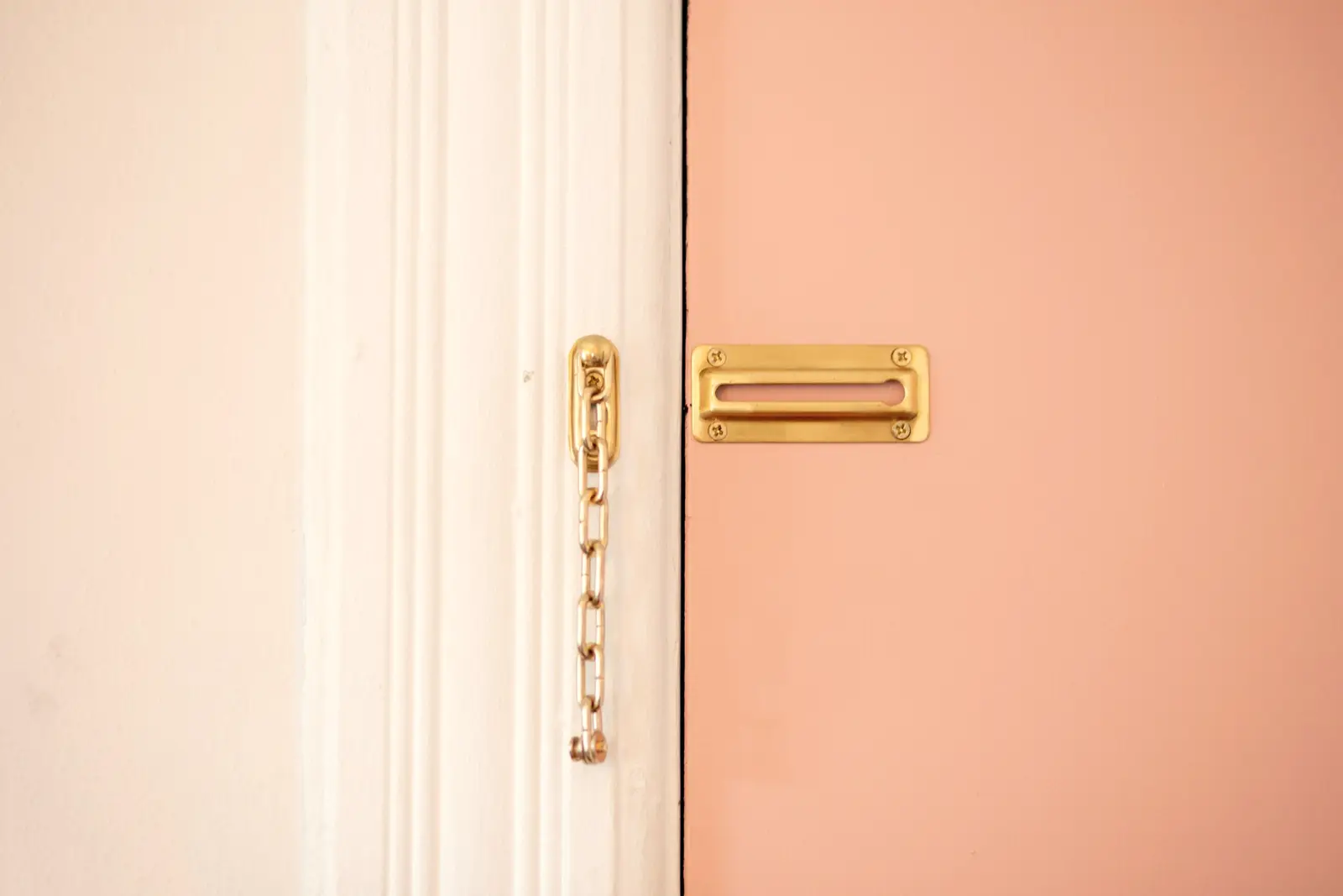 Porte d’entrée entrebâillée, chaîne de sécurité tendue et boîte aux lettres en laiton vissée sur le panneau.