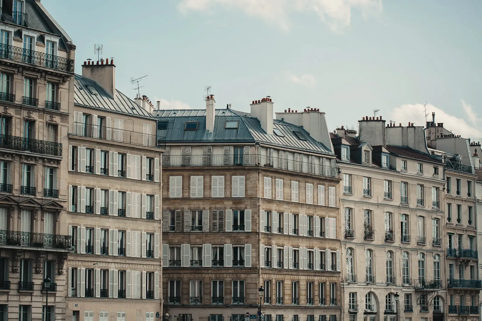 Alignement d’immeubles anciens : façades en pierre, volets persiennes, toits en zinc et souches de cheminées.