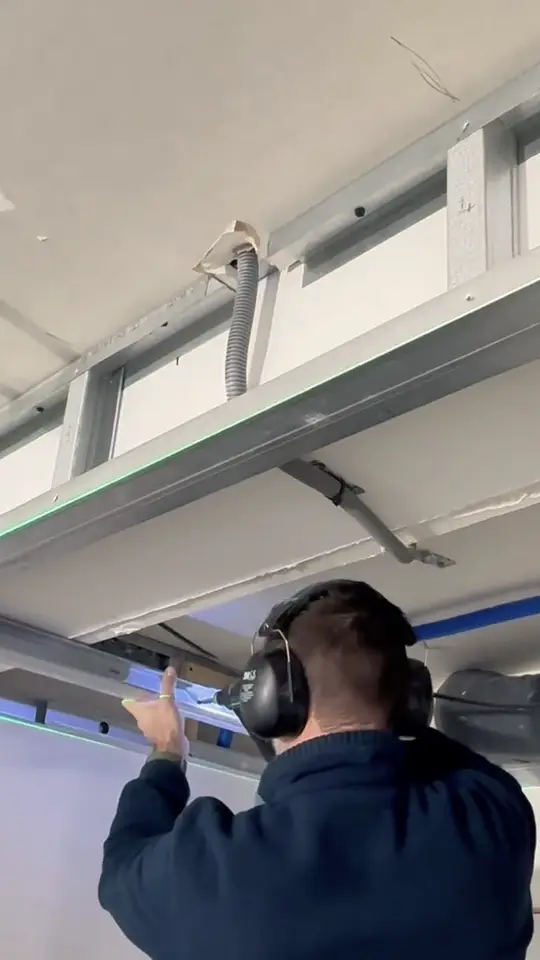 Ossature métallique de faux plafond contournant une poutre, alignée sur un trait de laser vert.