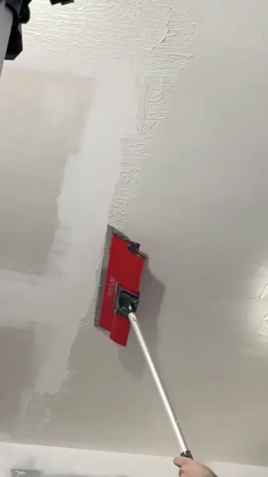 Lisseuse à manche télescopique tirée sur un plafond en plaques, entre une zone déjà enduite et le support brut.