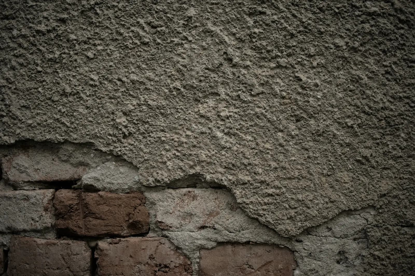 Bas d’un mur dont l’enduit s’est détaché en plaques, découvrant la brique et les joints de mortier.