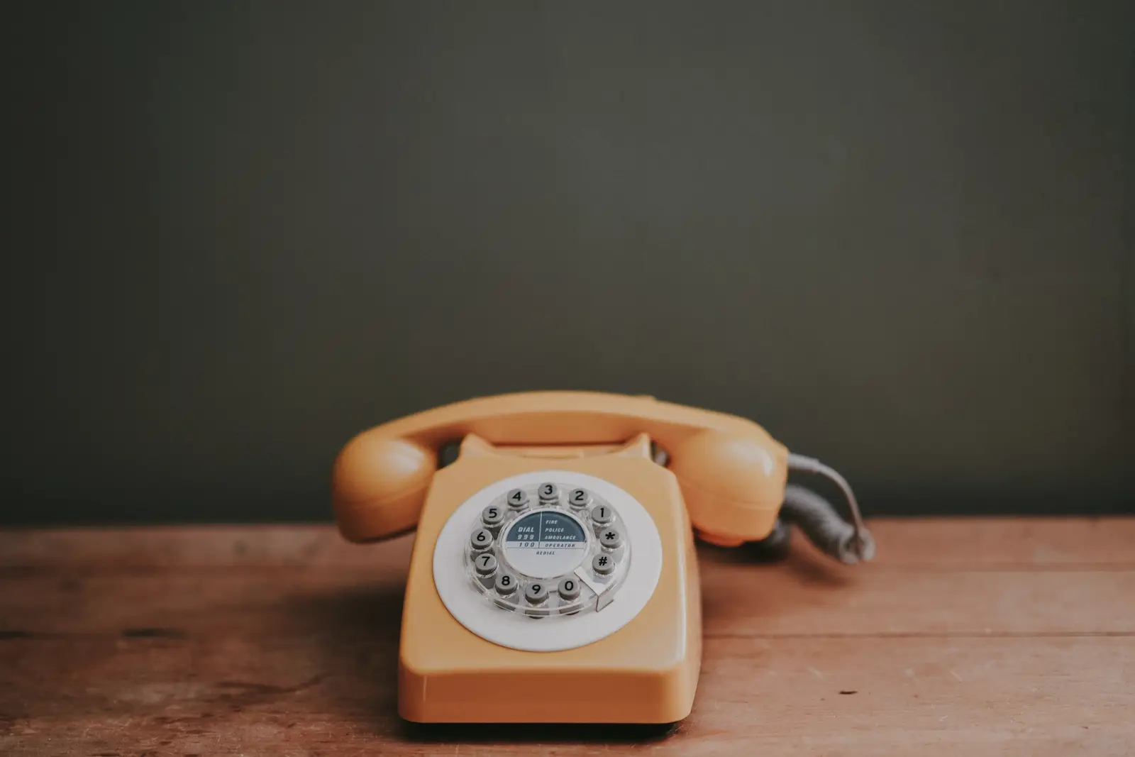 Téléphone à cadran posé sur une table en bois, combiné raccroché, devant un mur sombre.