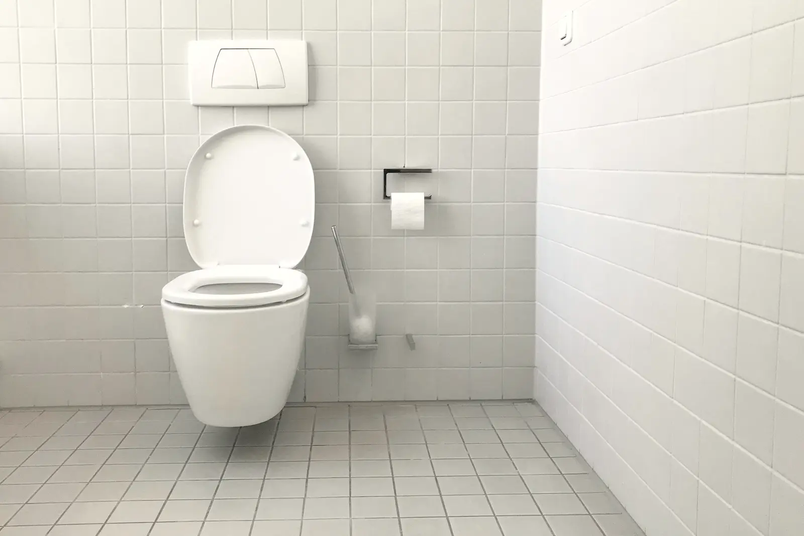 WC suspendu sur son bâti-support, plaque de commande encastrée au-dessus, carrelage blanc du sol au mur.