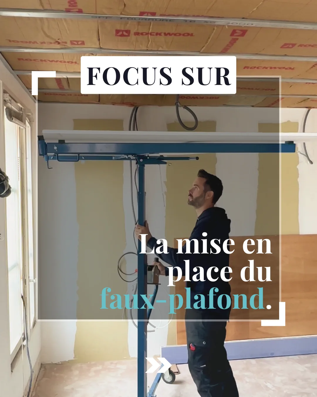 Ossature de faux-plafond en cours de montage au lève-plaque, laine de roche déjà posée entre les solives.