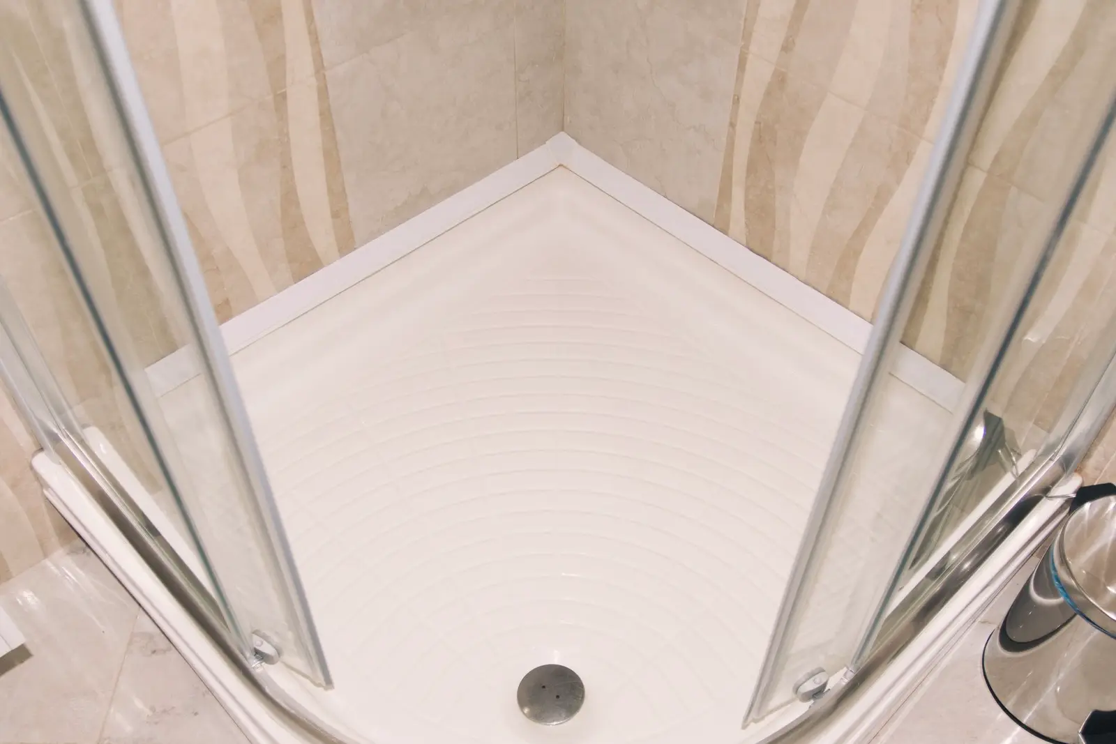 Receveur de douche d’angle et sa bonde centrale, vus de dessus à travers les portes vitrées refermées.