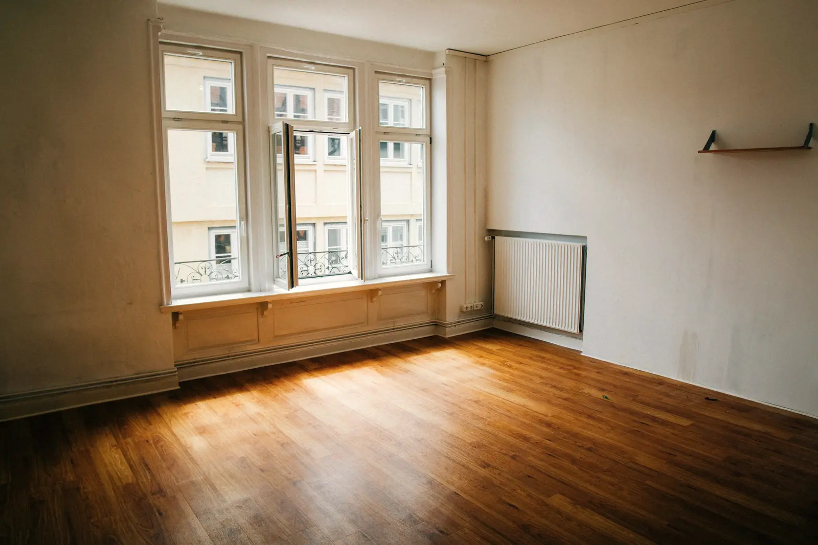 Pièce vide en fin de chantier : parquet posé, murs enduits, radiateur raccordé et fenêtre ouverte sur la rue.