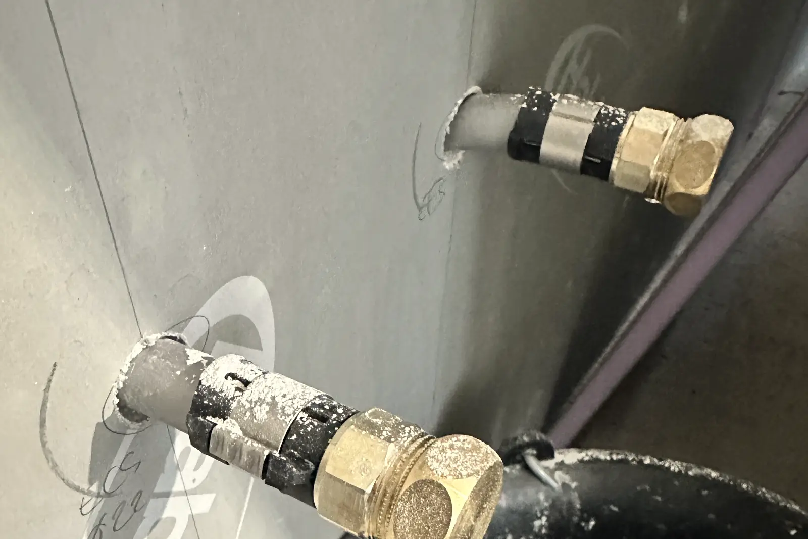 Deux attentes d’alimentation en eau bouchonnées au laiton, sortant d’une cloison ouverte au ras d’une évacuation existante, avec le diamètre noté au crayon sur la plaque.