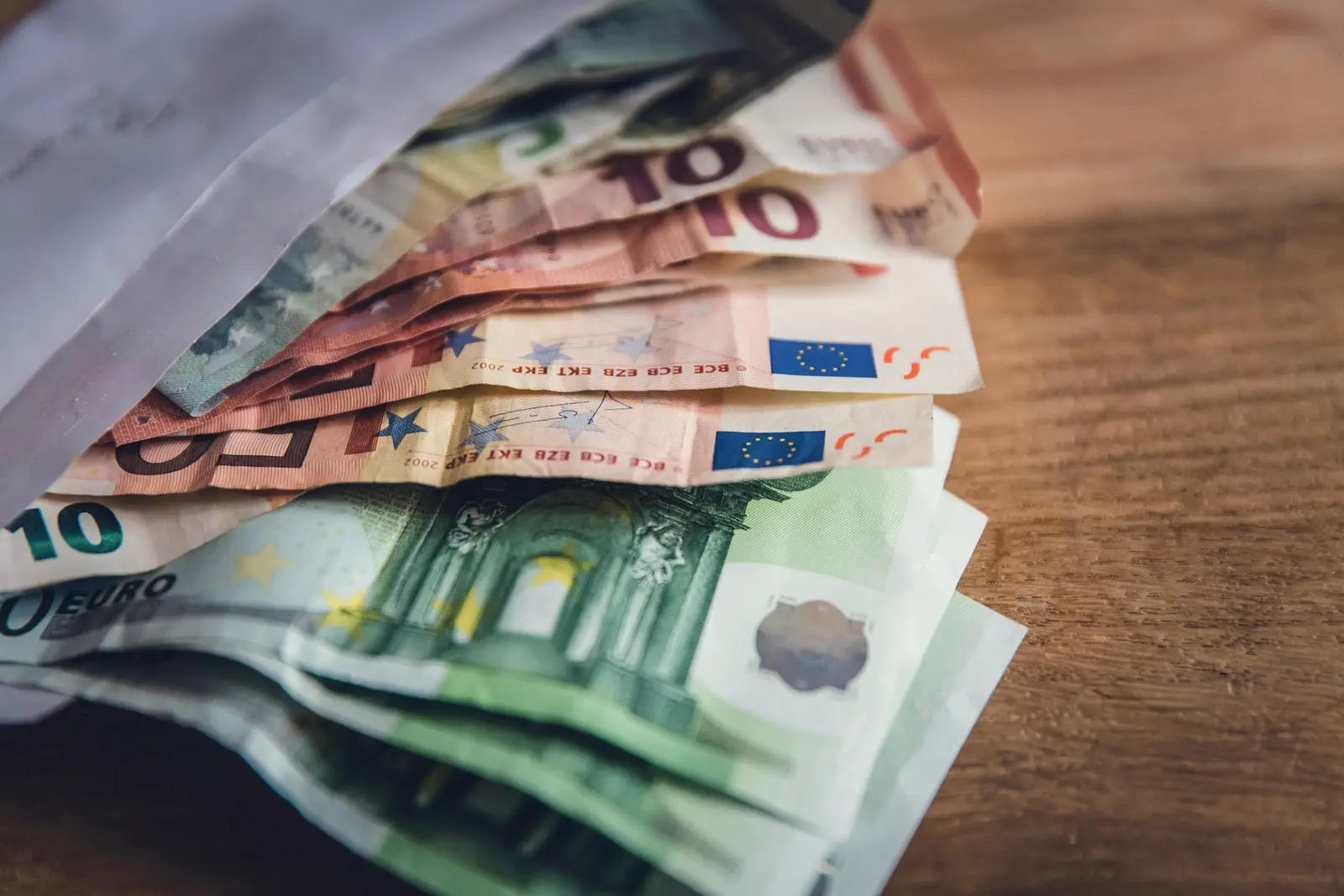 Billets en euros dépassant d’une enveloppe ouverte, posée sur une table en bois.